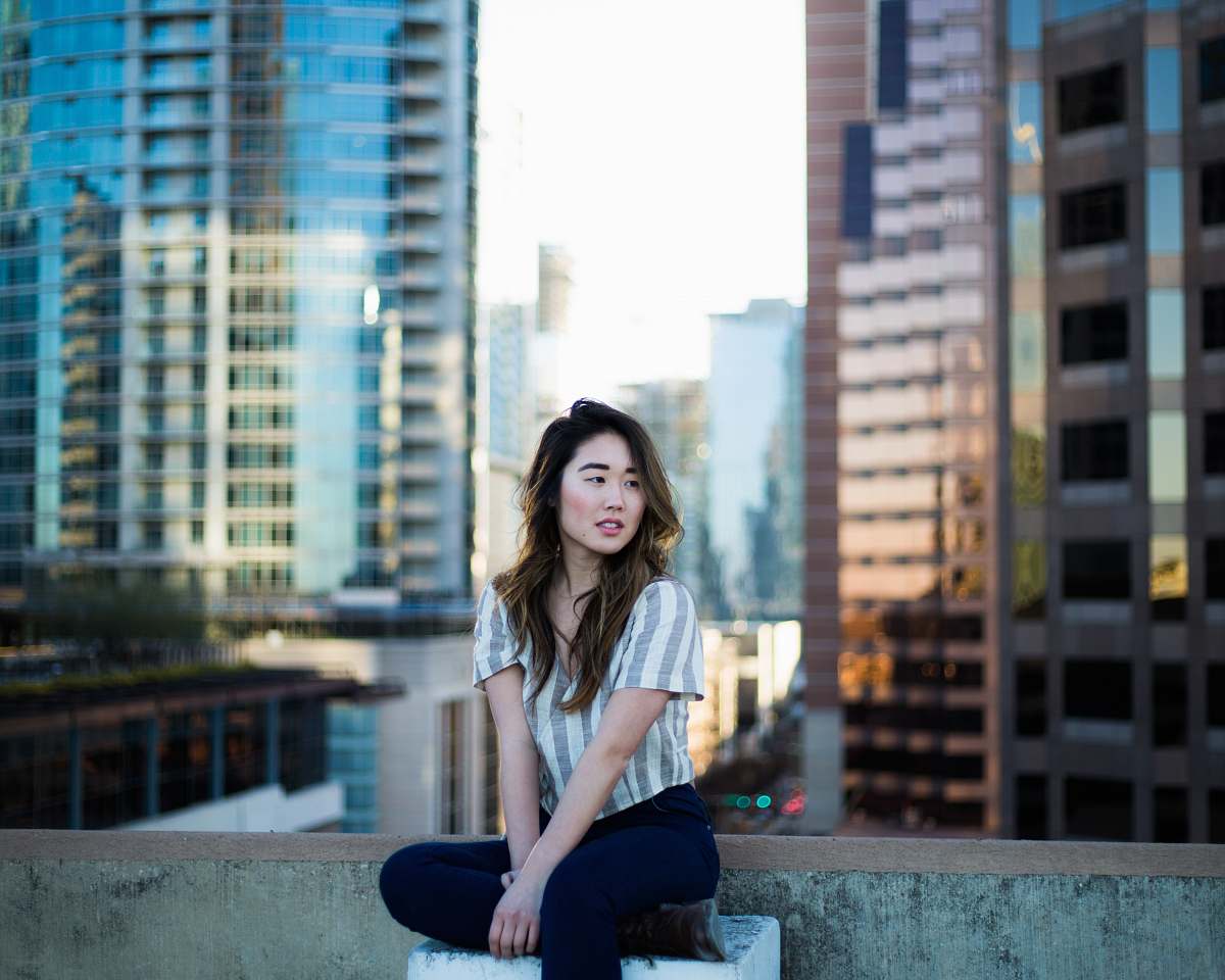 person selective focus photography of woman in gray shirt sitting near building edge people