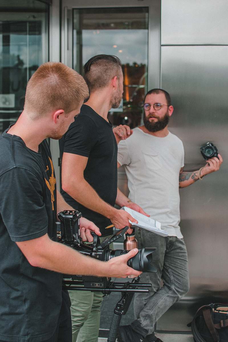 person three men holding cameras beside grey building people