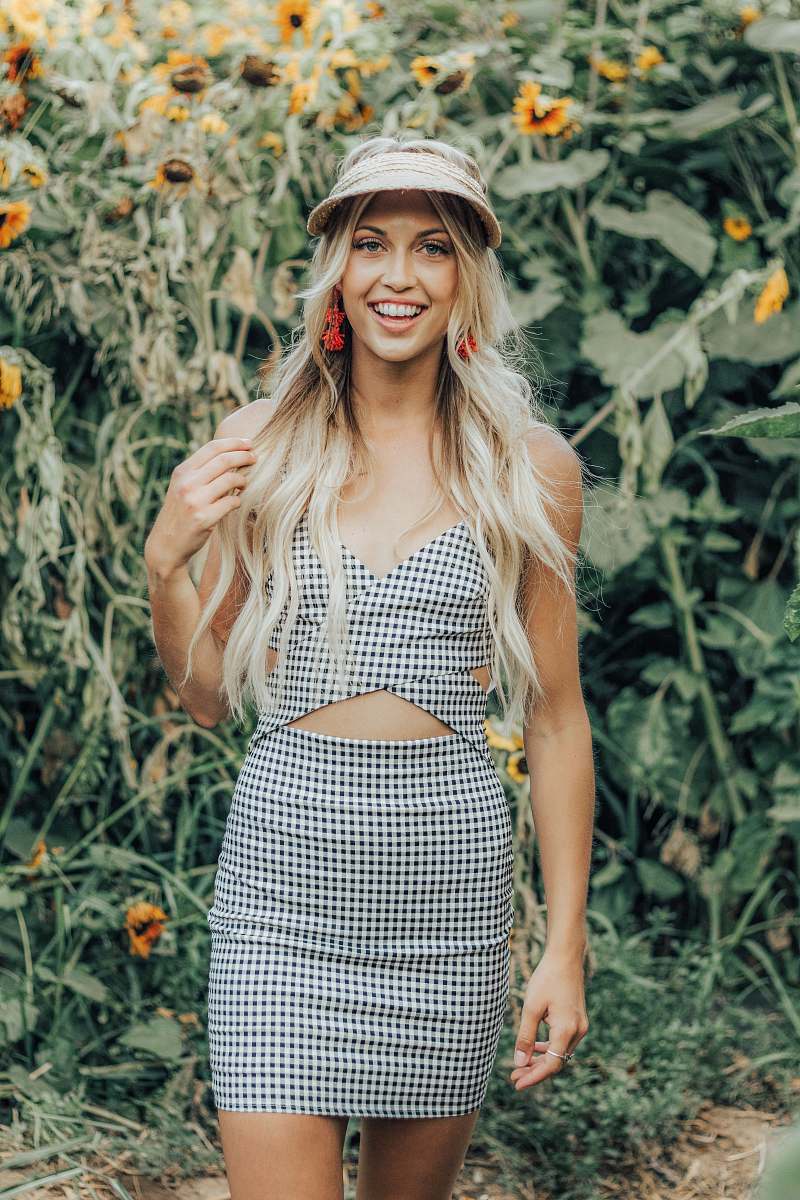 person woman in black and gray checked tank dress stands near sunflower people