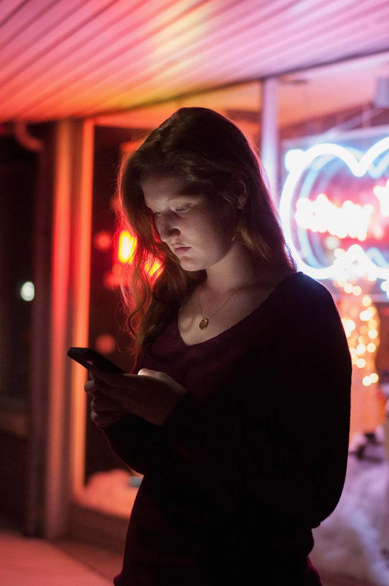 person woman using smartphone in front of red and blue lighted glass store people