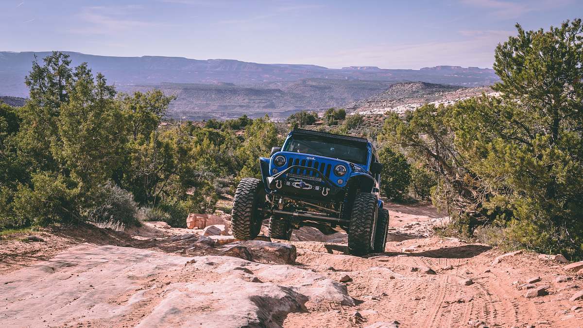 wheel blue Jeep Wrangler going up rocky sloped dirt road transportation