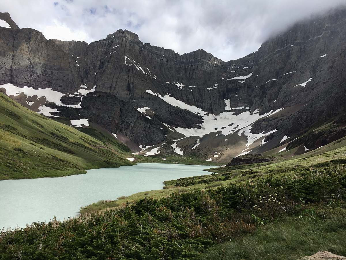 nature calm river between green grass field in distance gray rugged mountain under white cloudy sky daytime snow