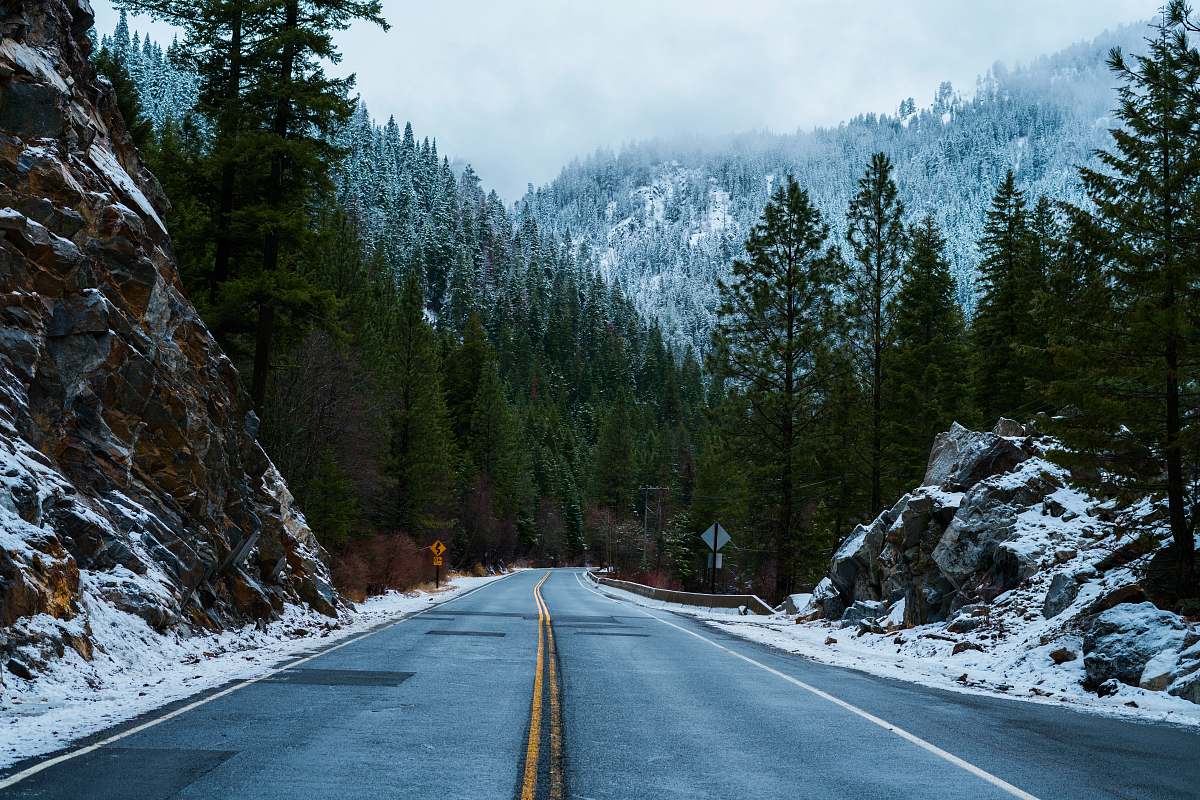 road gray road pavement in between mountain and trees mccall