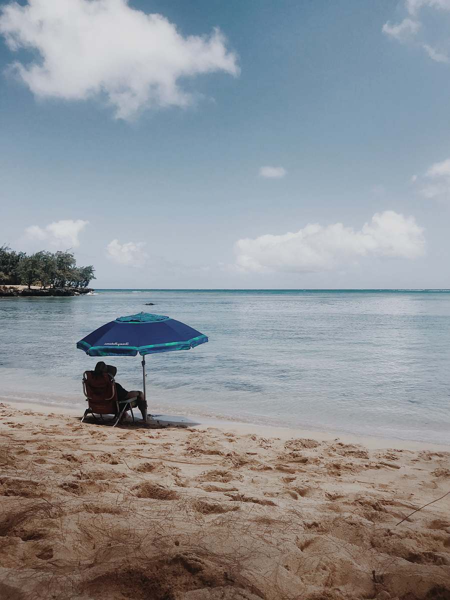 water person sitting on chair under blue umbrella on beach during daytime shoreline