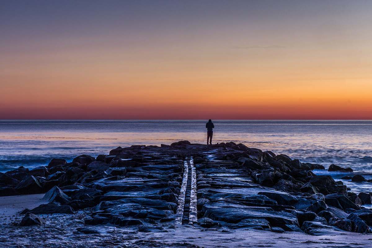 ocean person standing on rocks silhouette coast