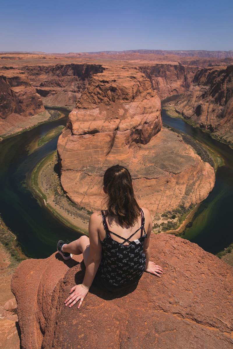 mountain photo of sitting woman in black camisole look down body of water near rocky hills canyon