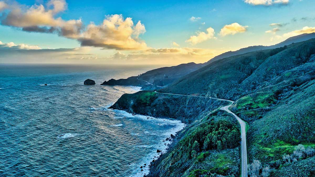 ocean road near a hill and body of water during daytime sea