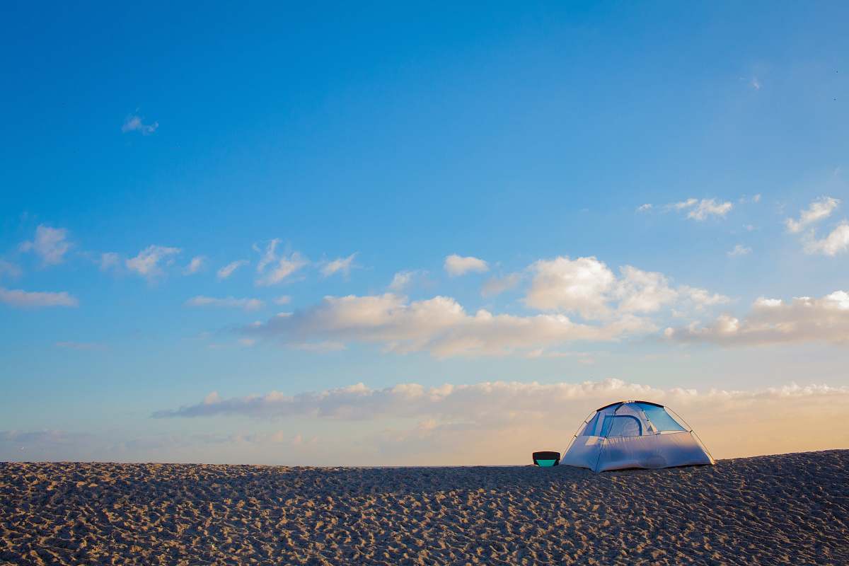 outdoors tent on sand under blue sky and white clouds tent
