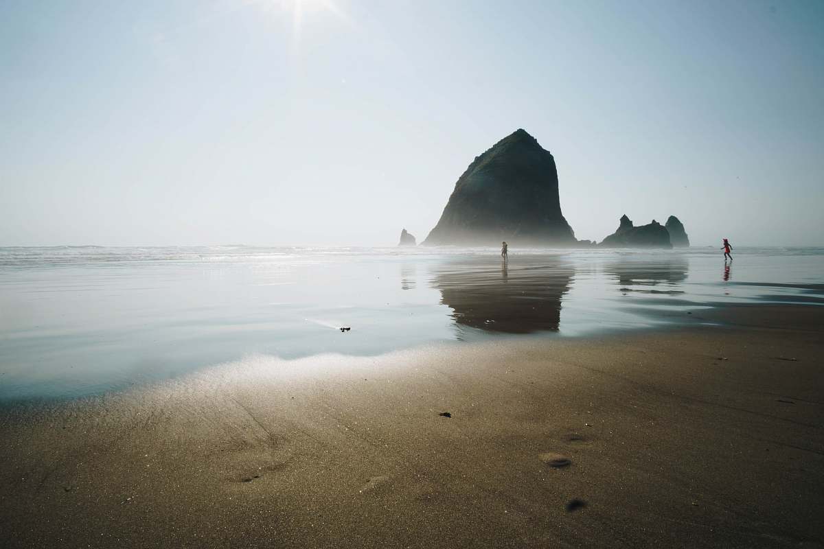 coast rock formation beside sea near people walking on shore at daytime sea
