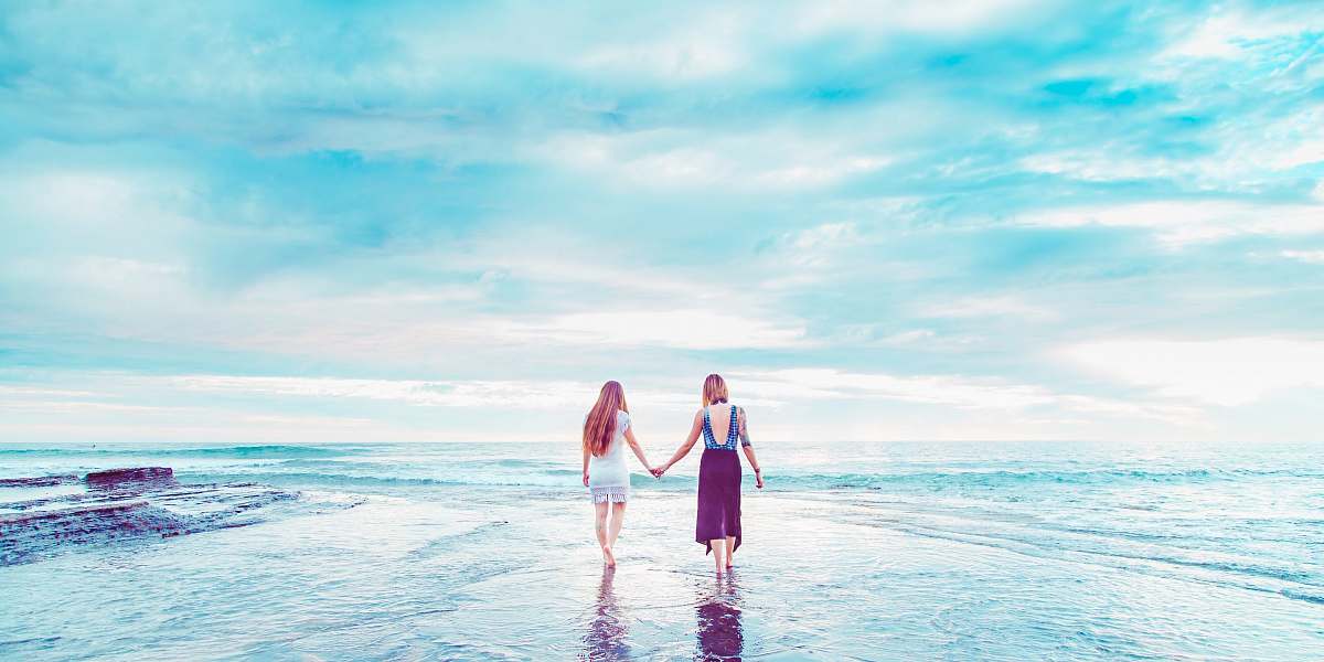 sea two women walking on shoreline holding hands san diego