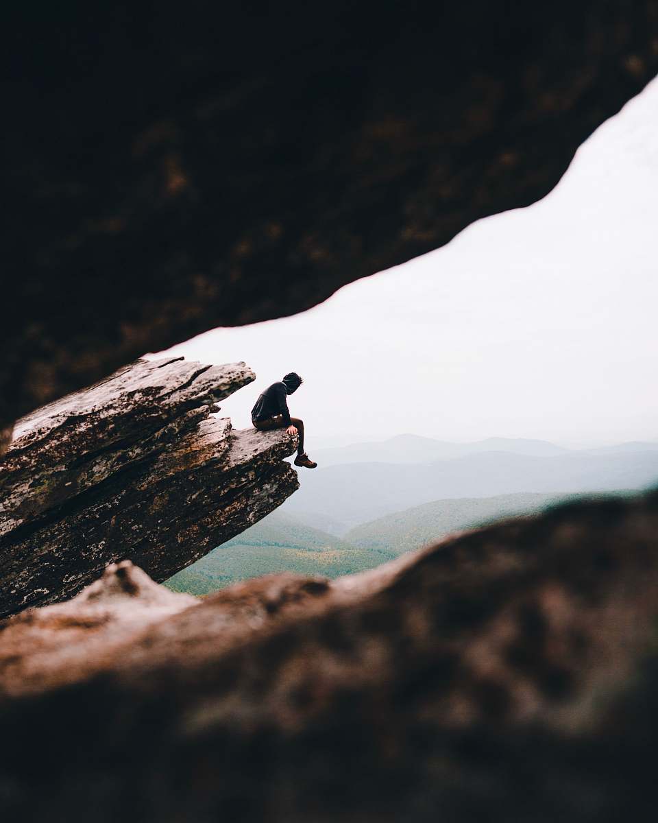 adventure selective focus photography of person sitting on cliff during daytime leisure activities