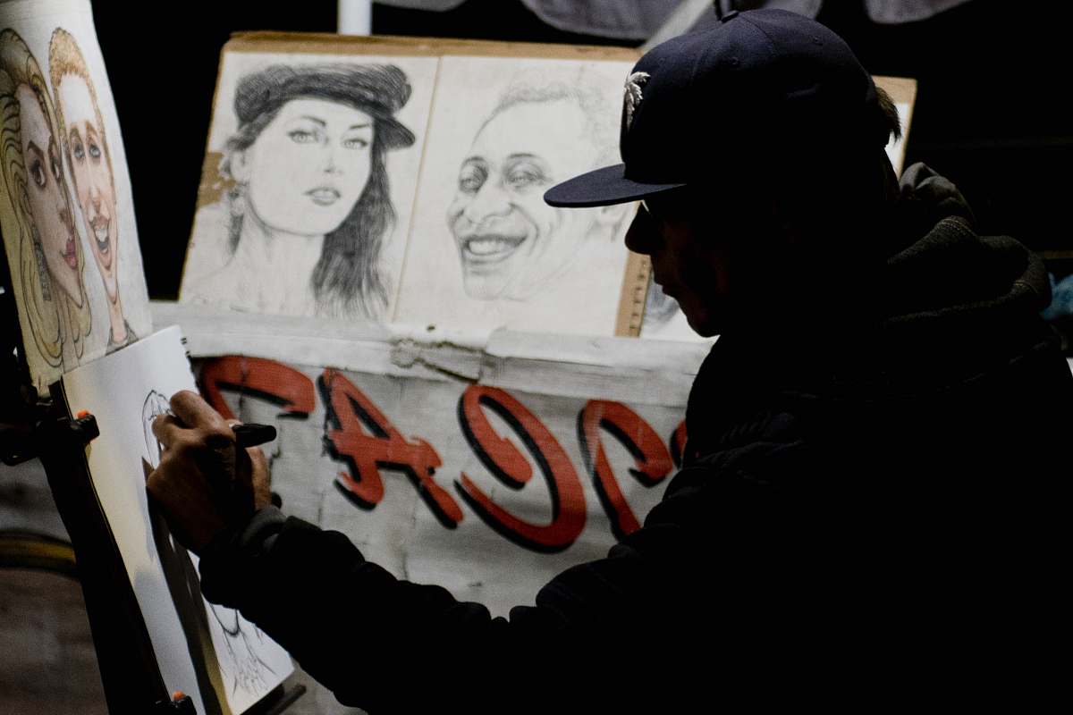 human man wearing cap sitting while doing portrait sketches person