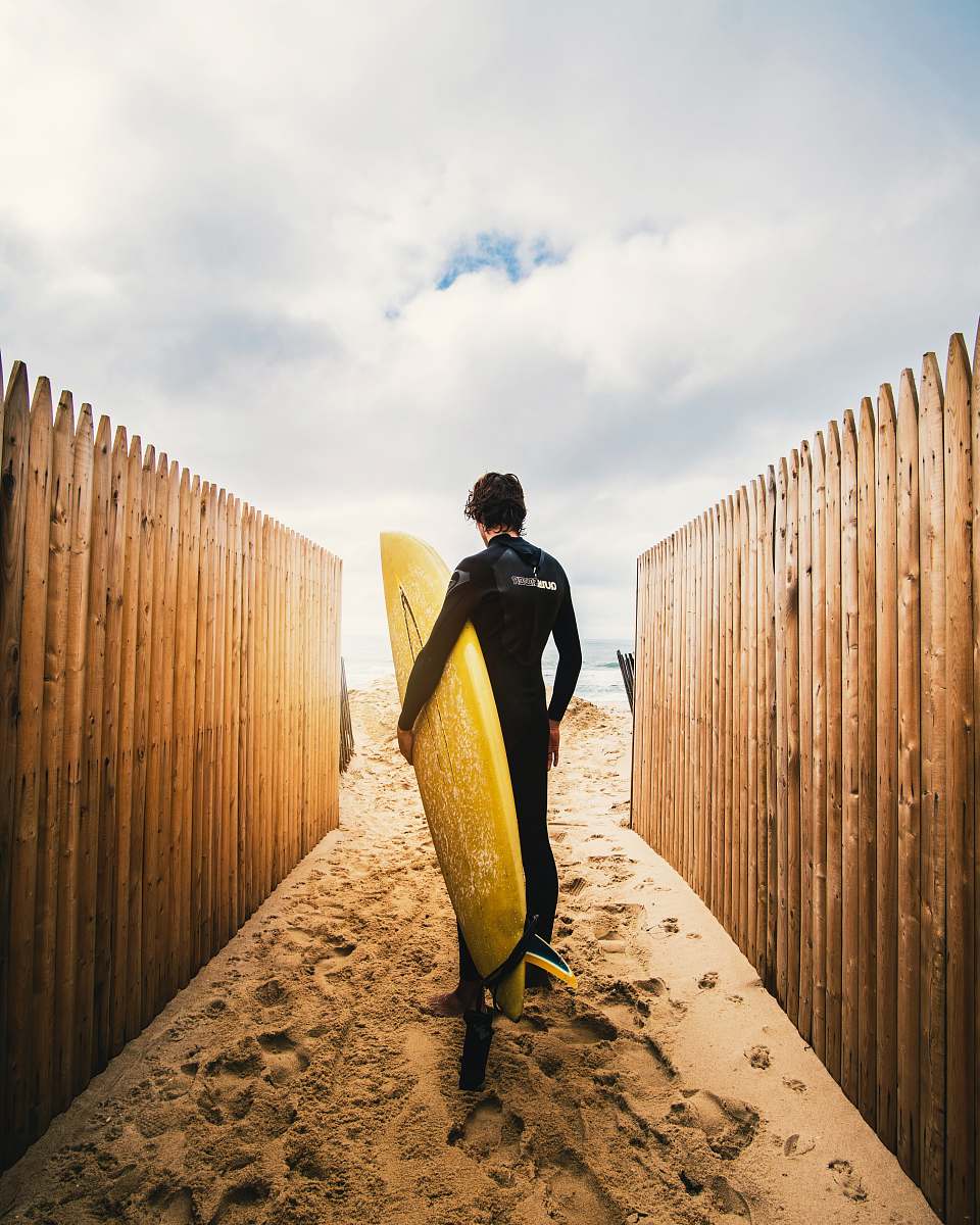 human person standing between privacy fences while holding yellow surfboard during daytime person
