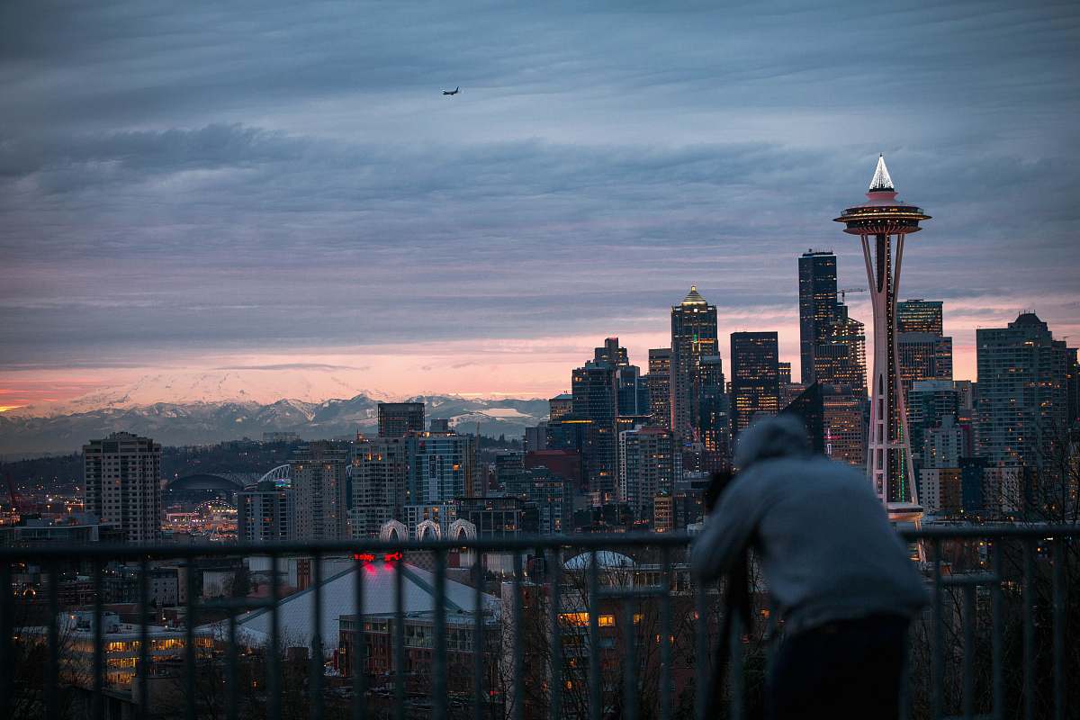 person photo of person wearing grey pullover hoodie taking a photo of concrete buildings under cloudy sky human