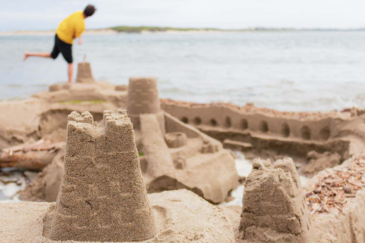 person selective focus photography of sand castle near man standing on seashore human