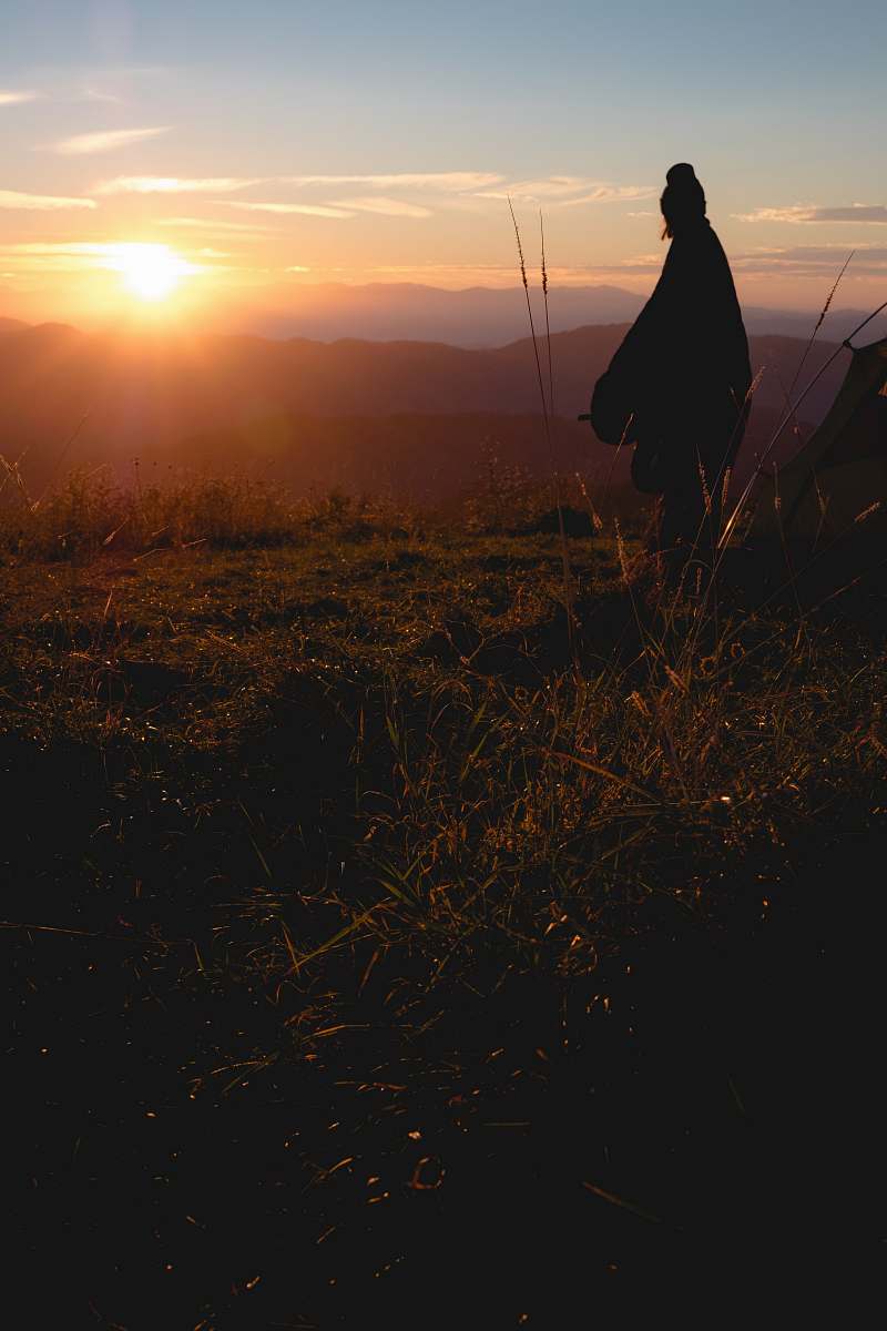 human silhouette photo of person wearing robe standing on hill person