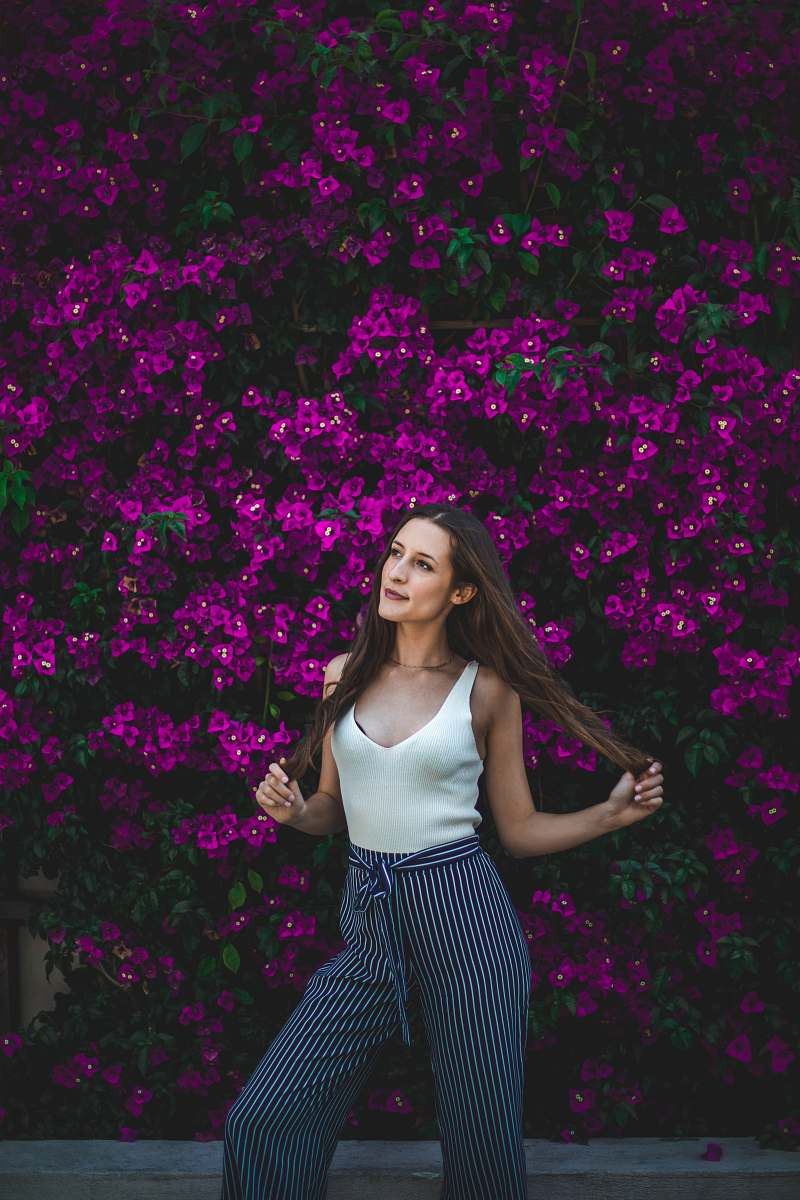 human smiling woman holding her hair in front of purple flowers during daytime person