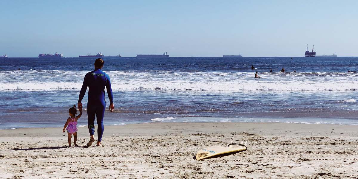 human man holding girl while standing on beach people