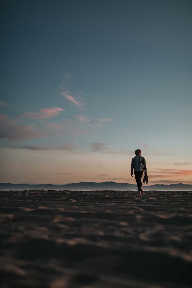 human man walking on sand while holding his footwears people