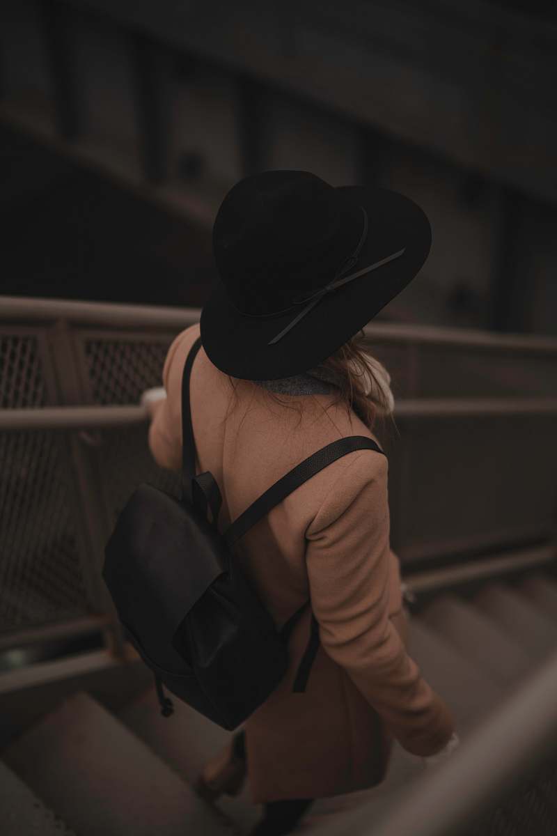 people person carrying black backpack while walking downards of stair hat