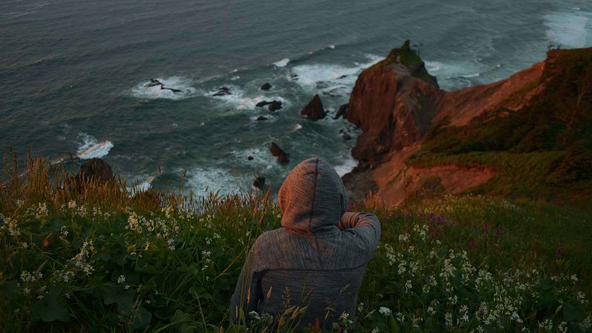 human person sits on grass front of ocean people