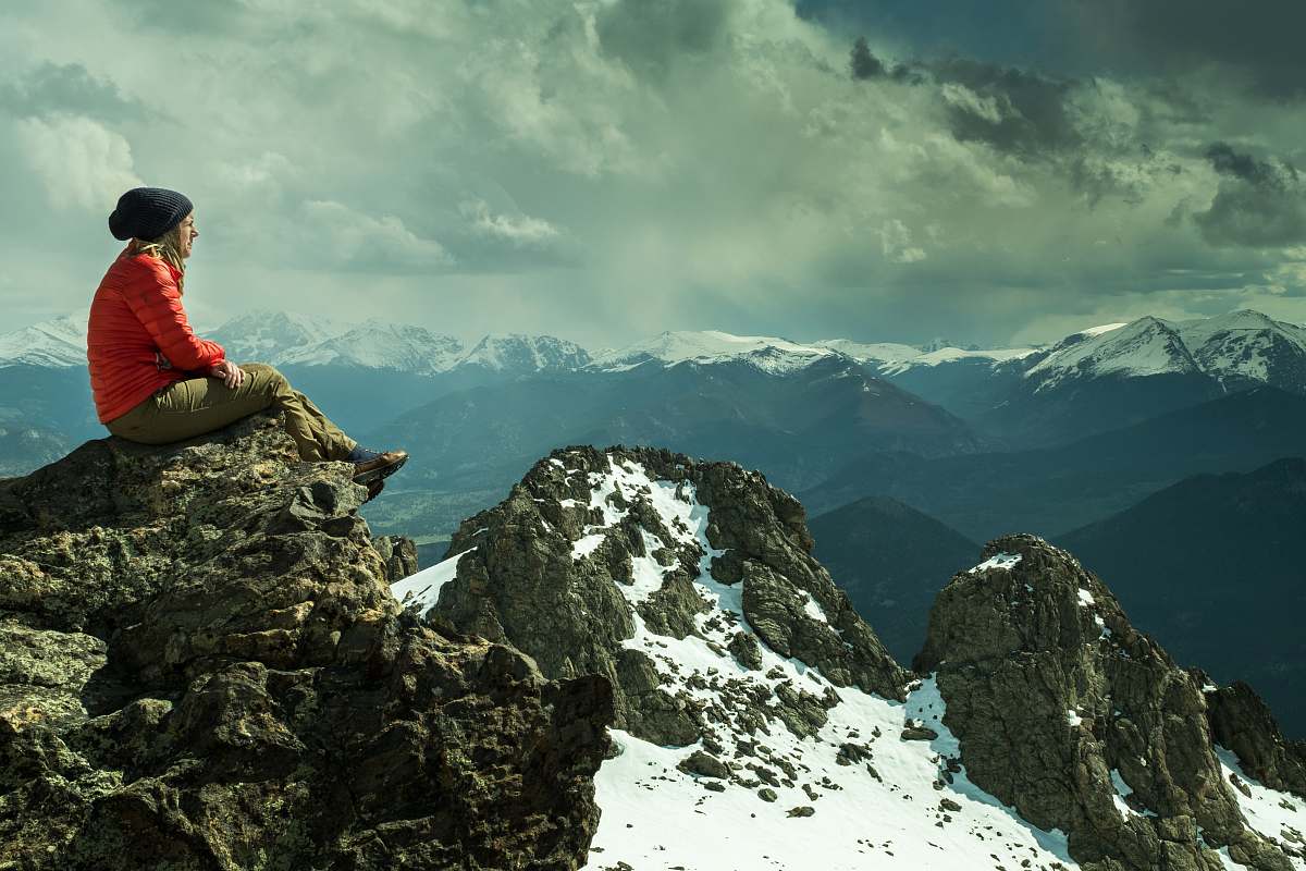 outdoors person sitting on rock across snow covered mountain under cloudy sky mountain