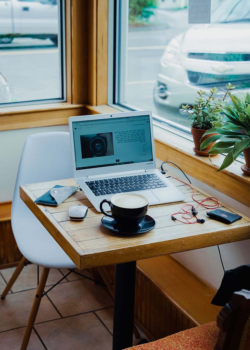 laptop cup of coffee, laptop computer, and red earphones plugged in laptop on brown wooden table desk