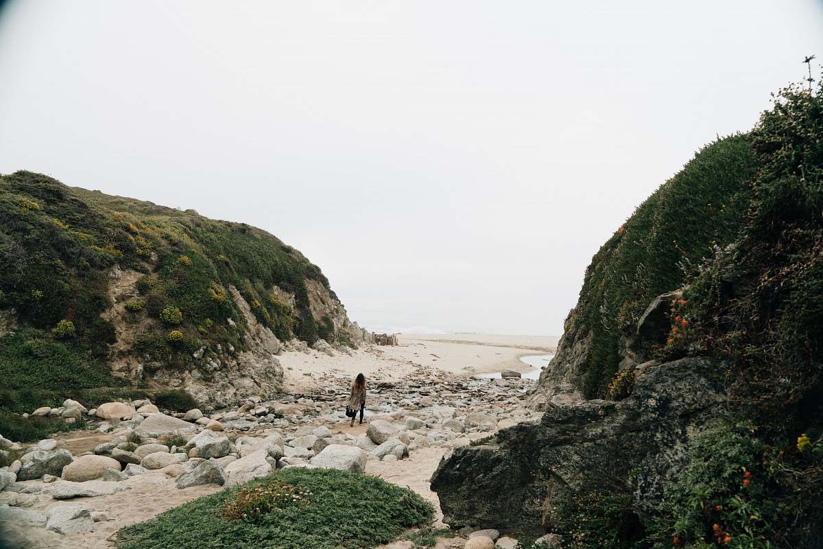 nature person in black shirt standing on brown rock near body of water during daytime outdoors