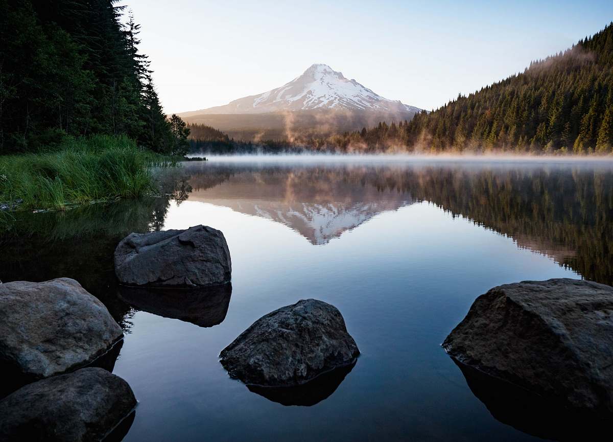 water calm body of water with rocks near trees and mountain tree