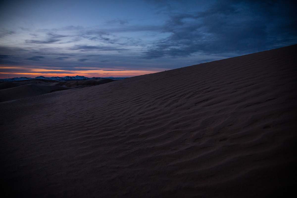 Experience the captivating beauty of a vast desert landscape featuring golden sands and majestic dunes, set against a striking dark orange sky. This stunning scene captures the essence of tranquility and the raw power of nature, making it perfect for travel brochures, environmental awareness campaigns, or as a backdrop for artistic projects. Ideal for anyone looking to evoke feelings of adventure, solitude, or the serene beauty of arid climates.