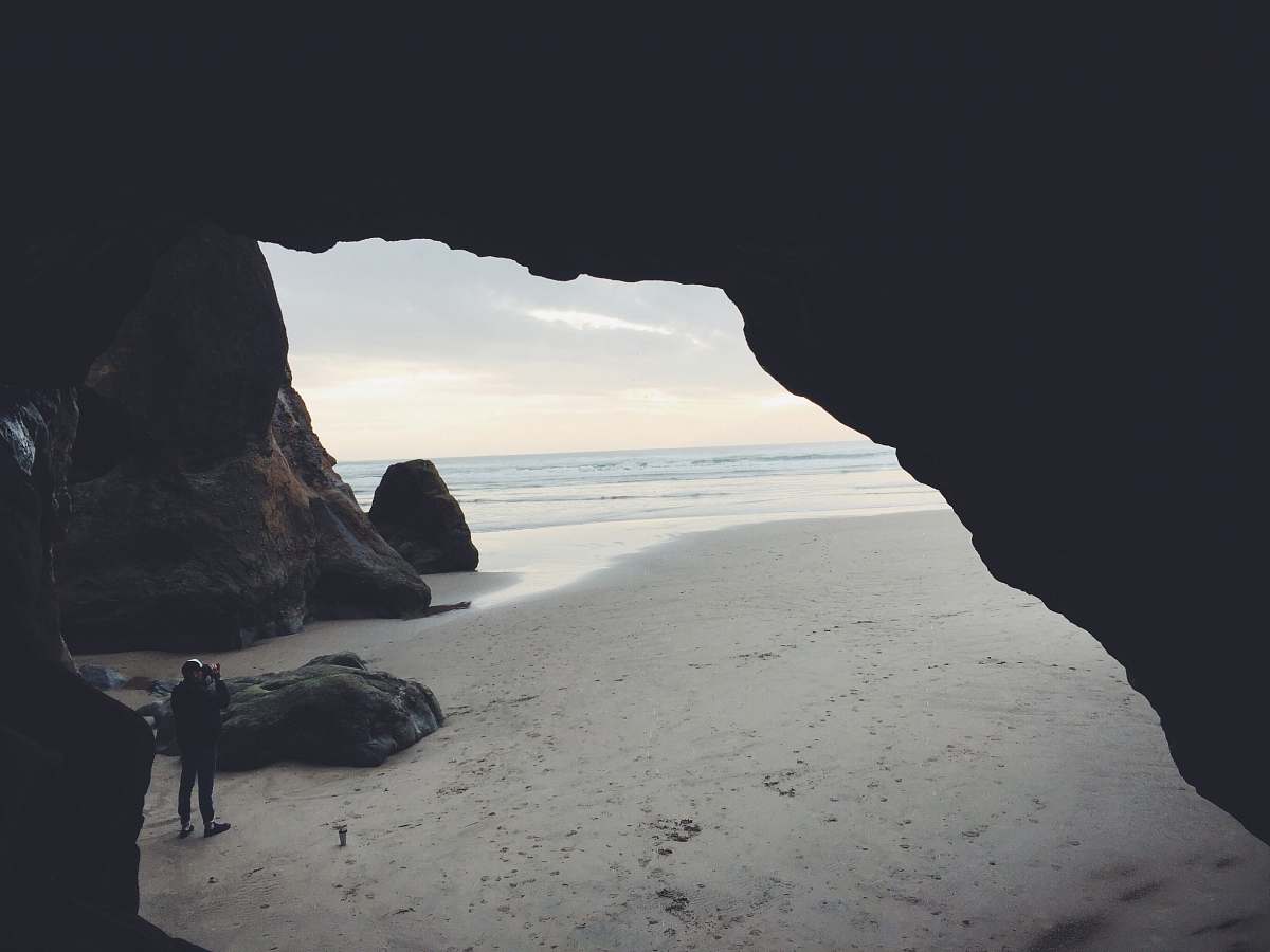 cave person taking picture beside cave ocean