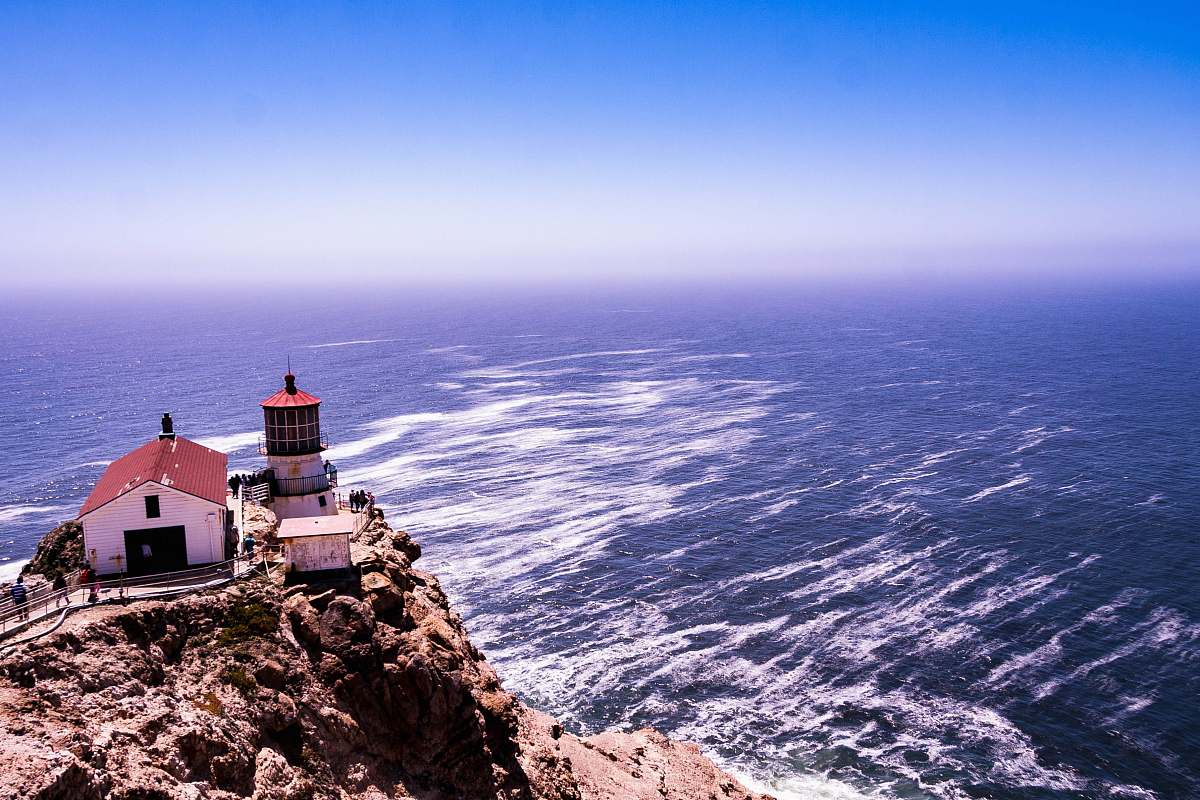 coast white and red shed beside lighthouse on hill overlooking the sea ocean