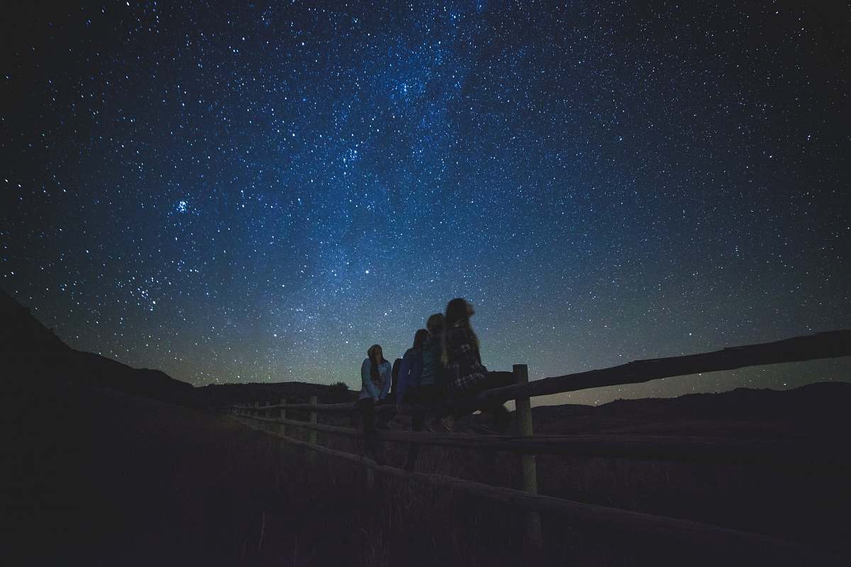 night several women sitting on fence watching milky way astronomy
