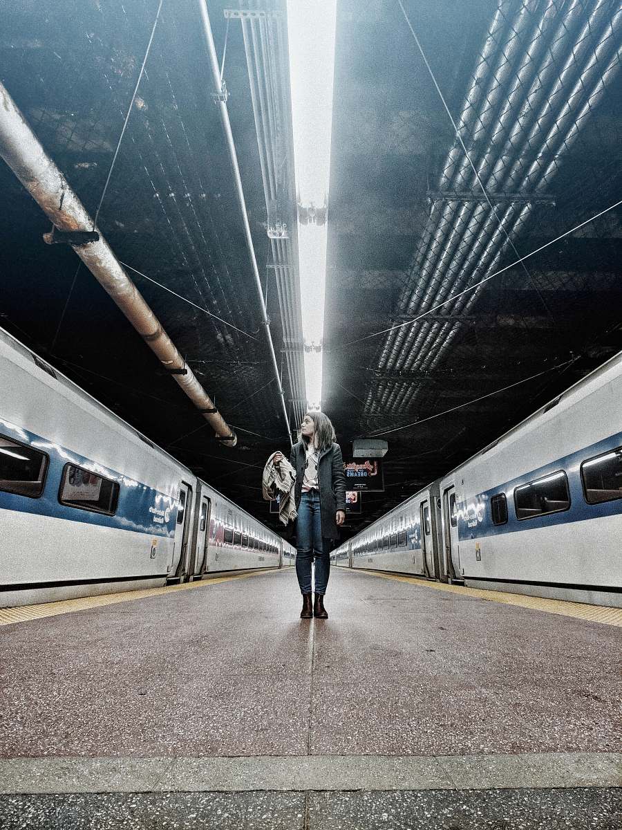 transportation woman standing in the middle of gray trains inside train station vehicle