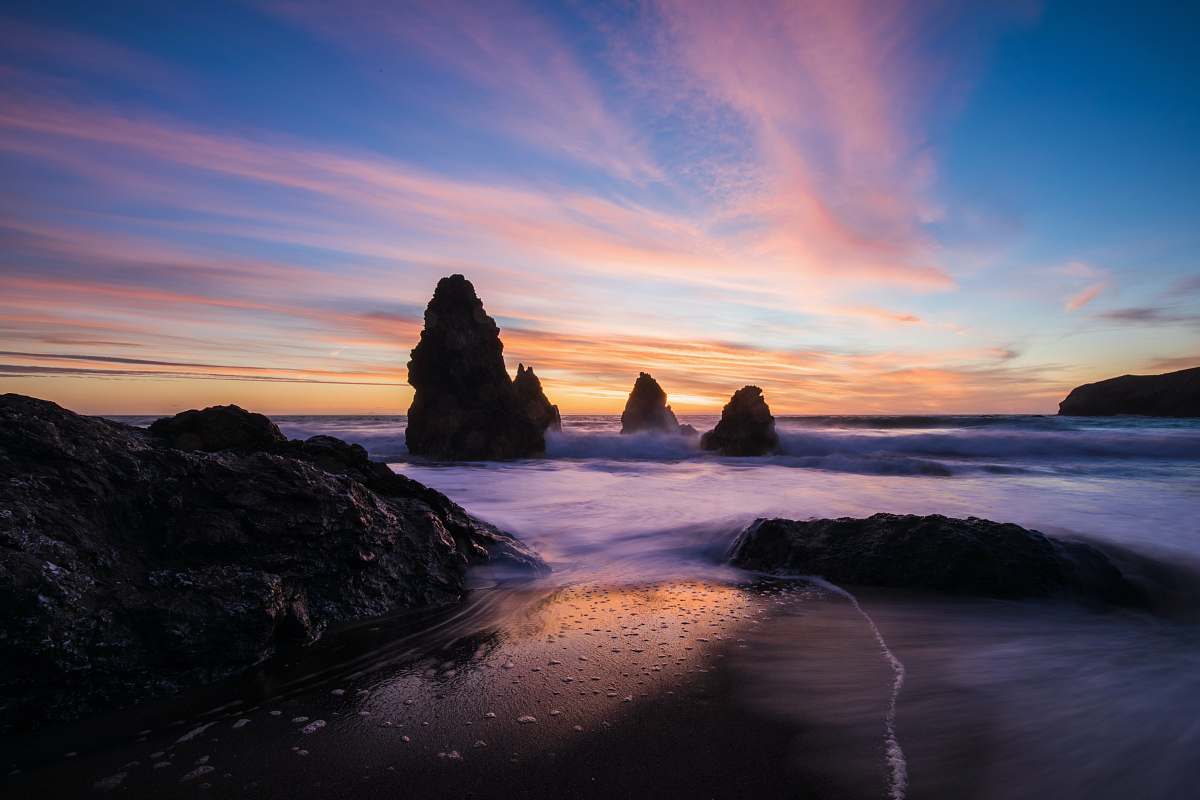 ocean rock monument beside water with cloudy sky sunrise