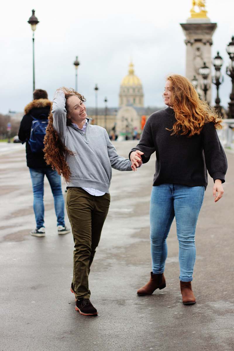 clothing two women holding hands together while walking on road during daytime footwear