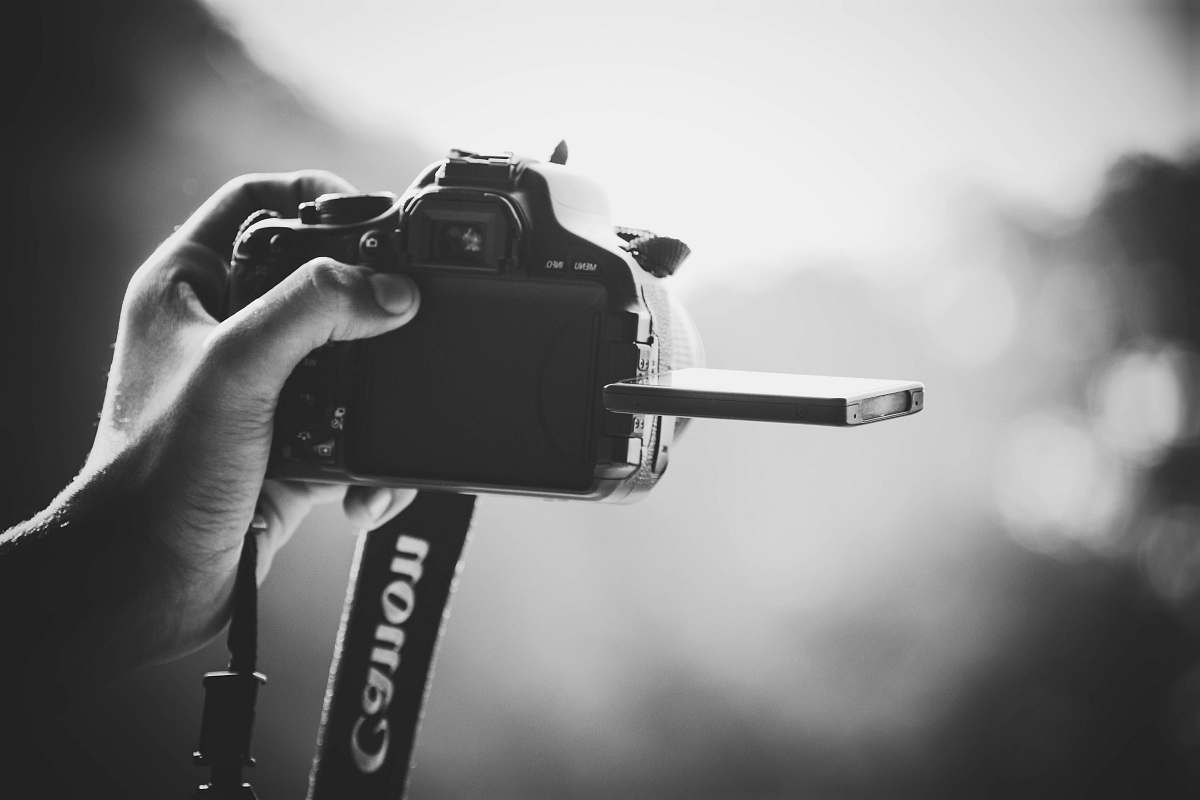 camera grayscale photography of person holding Canon DSLR camera canon