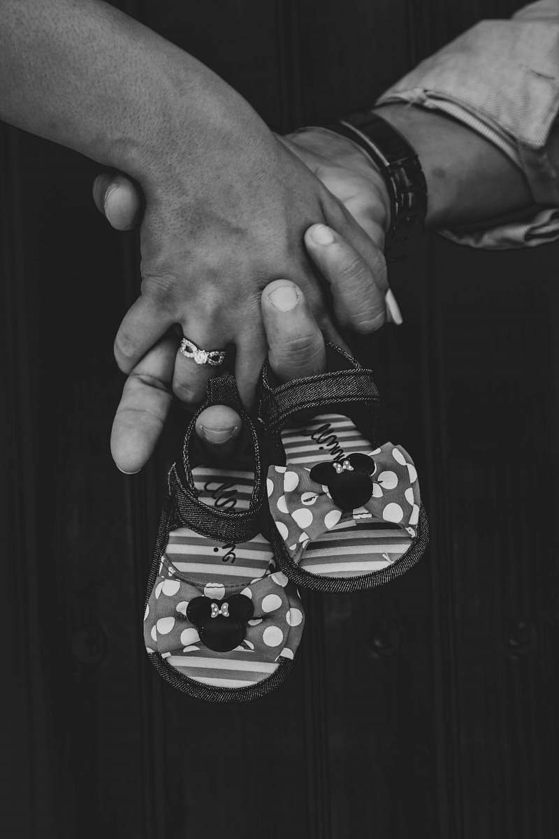 apparel grayscale photography of two person holding hands holding toddler shoes clothing