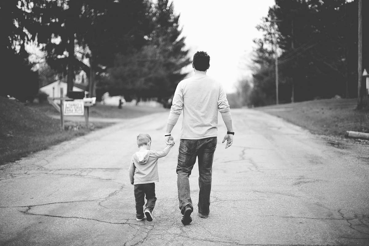 grey man holding baby's hand walking