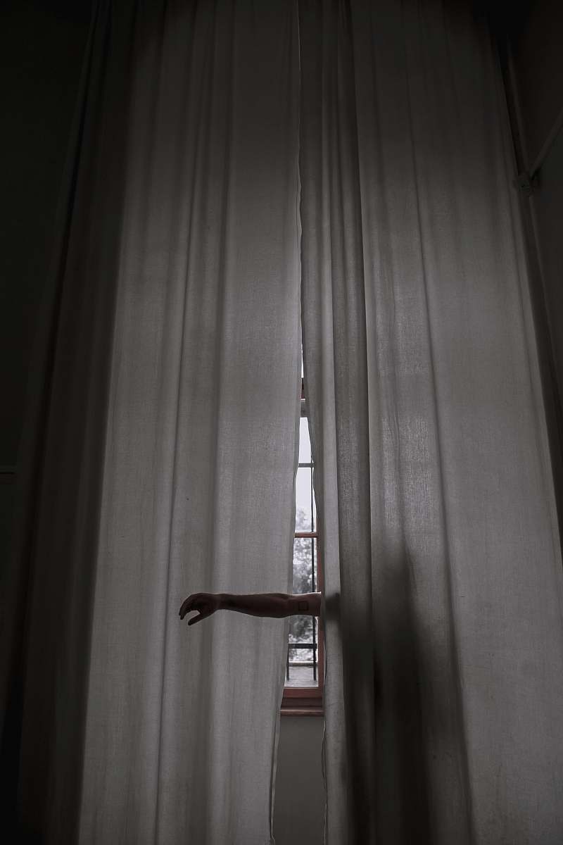 dark person standing beside the curtain and rising their arms grey