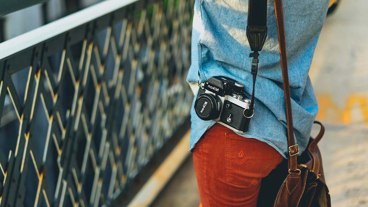 photographer person carrying bag and camera facing fence bag