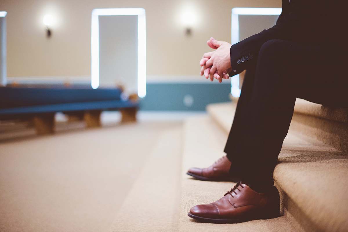 man man in black pants and pair of brown leather lace-up shoes sitting on brown carpeted stairs inside room sitting