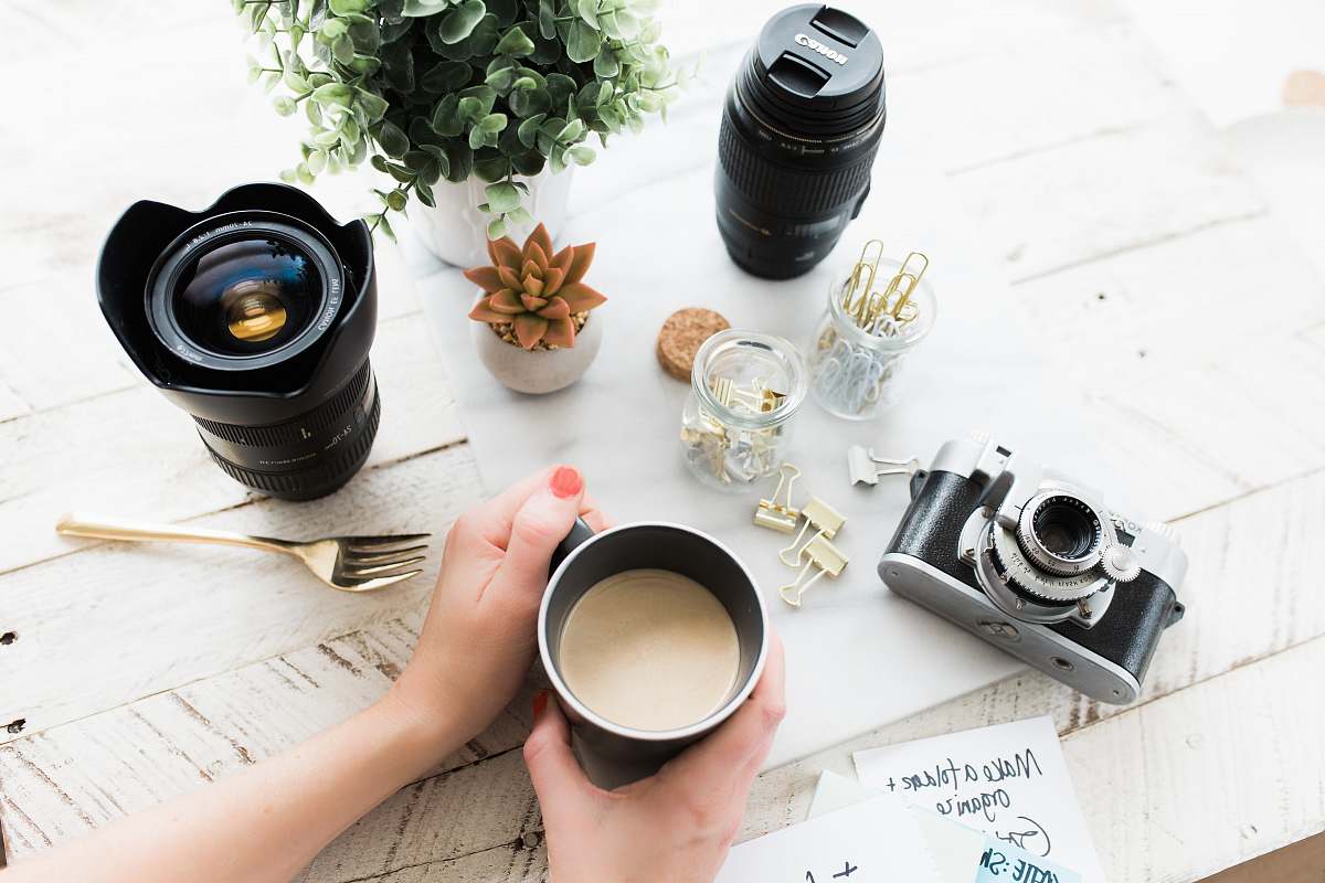 camera person holding black ceramic coffee mug beside black DSLR camera plant