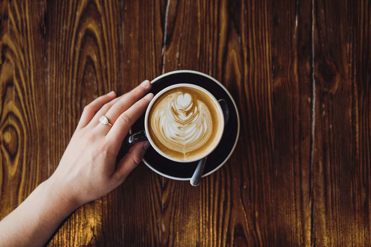 latte person holding cappuccino in teapot with saucer on table cup
