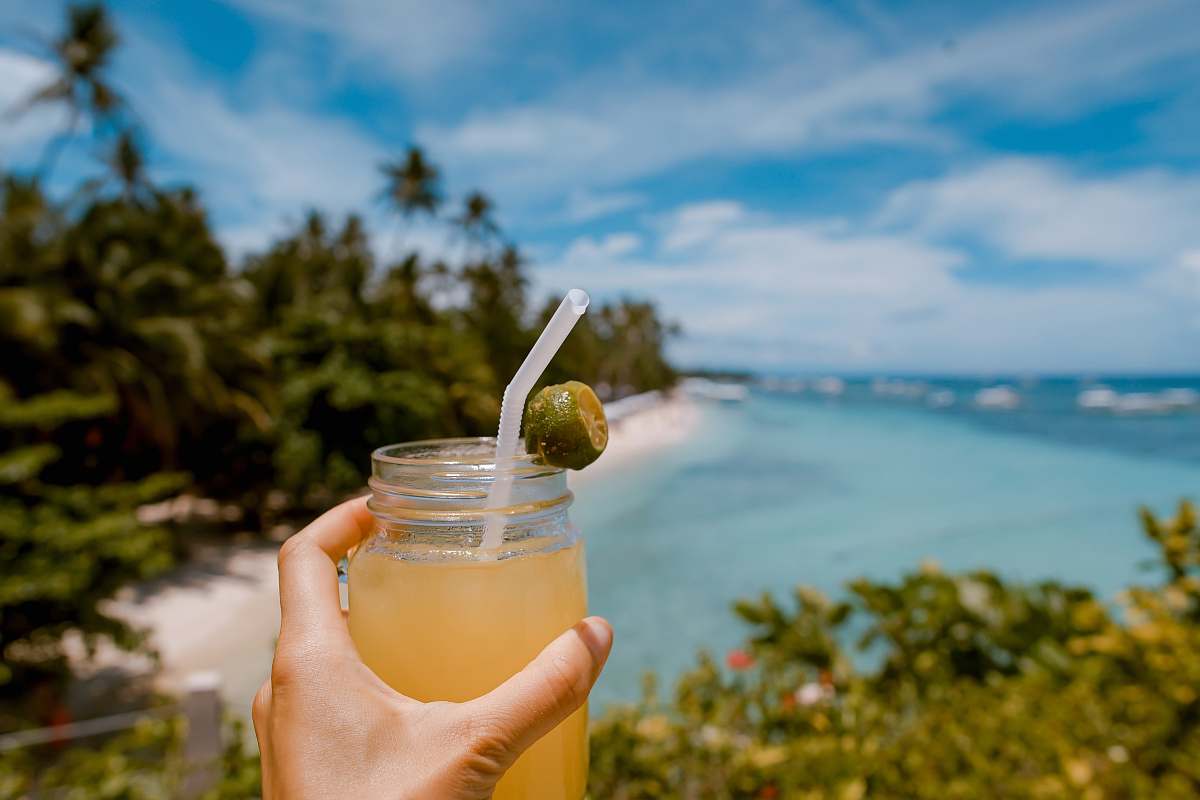 cocktail person holding mason jar with filled with juice at daytime alona beach