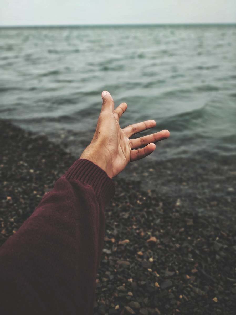 human person raising hand near body of water person
