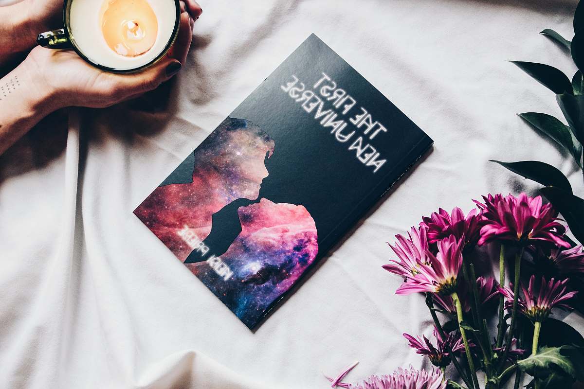 hand The First New Universe book on white textile flower