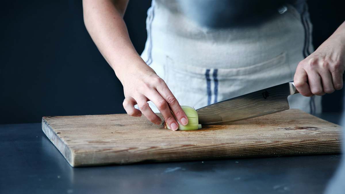 chef person slicing green vegetable on chopping board kitchen