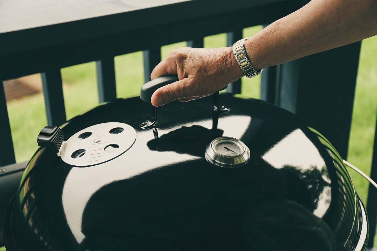 bbq person holding kettle grill's cover near balustrade barbeque