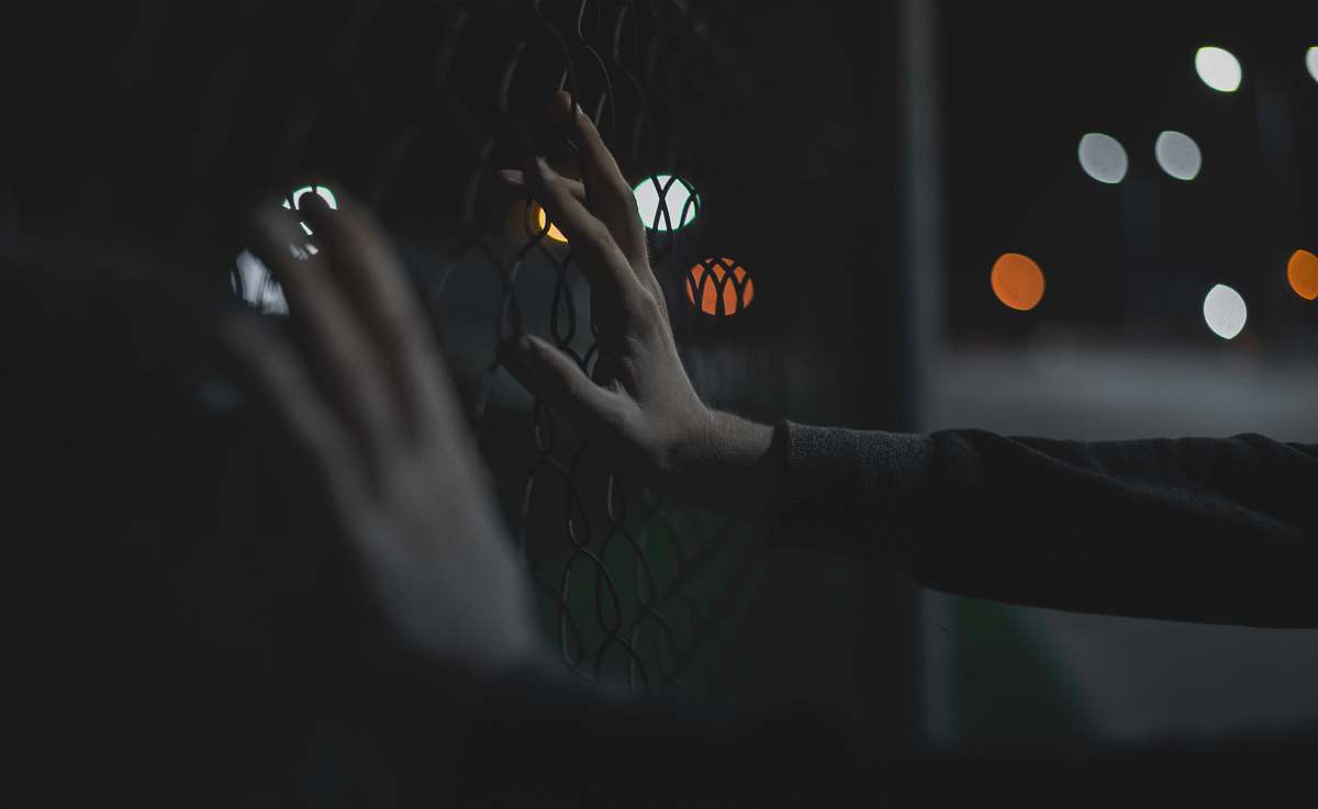 hands close-up photography of person grabing gray iron fence fingers